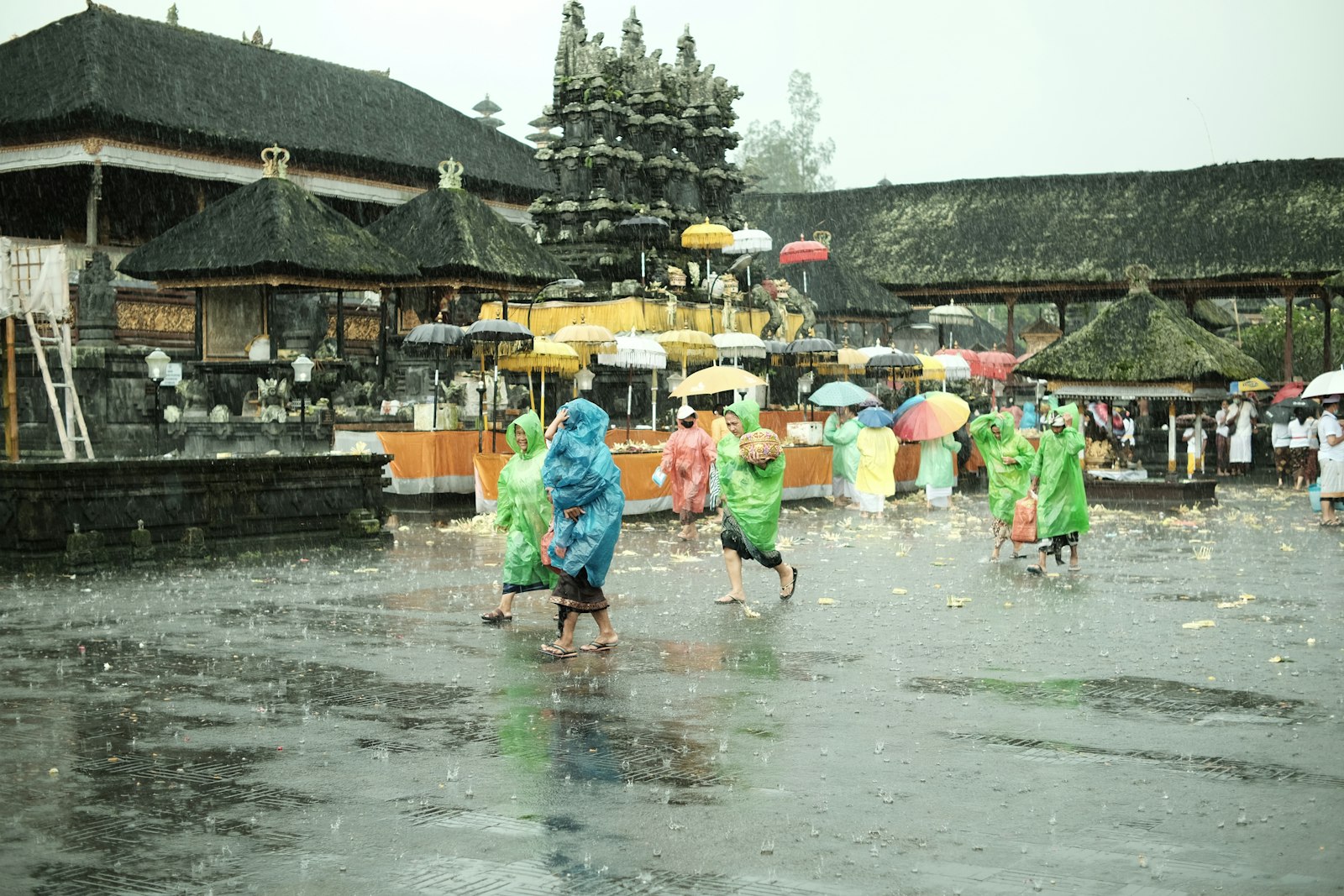 Yağmur altında şemsiyelerle Besakih Tapınağı'na yürüyen ziyaretçiler, Bali